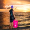 Female swimmer standing by the sea holding a pink buoy bag