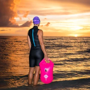 Female swimmer standing by the sea holding a pink buoy bag